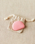 Hibiscus colored Cocoknits tape measure in a drawstring bag on a beige fabric background
