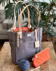 Gray tote bag with orange interior on a wooden table, accompanied by yarn and knitting needles.