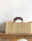 Woven basket with handles on a wooden surface against a white wall