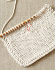 Knitted fabric with colorful stitch marker on wooden knitting needles on a beige background