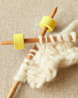 Knitting needles with white yarn on a beige fabric background