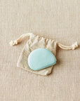 A biodegradable, plastic-free Cocoknits tape measure in a natural tone color, displayed on a beige background with a drawstring linen bag.