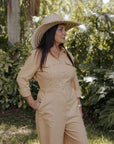 Person wearing a beige jumpsuit and hat standing in a garden