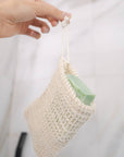 Woven agave soap bag with a green soap bar hanging from a hand in the shower