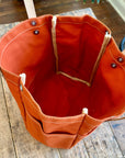 Orange tool bag on a wooden floor with plants in the background