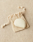 Linen colored Cocoknits tape measure on a beige drawstring bag against a beige fabric background