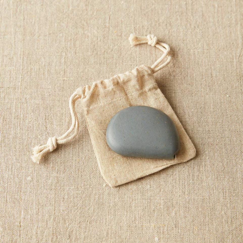 Stone colored Cocoknits tape measure on a beige drawstring bag against a beige fabric background