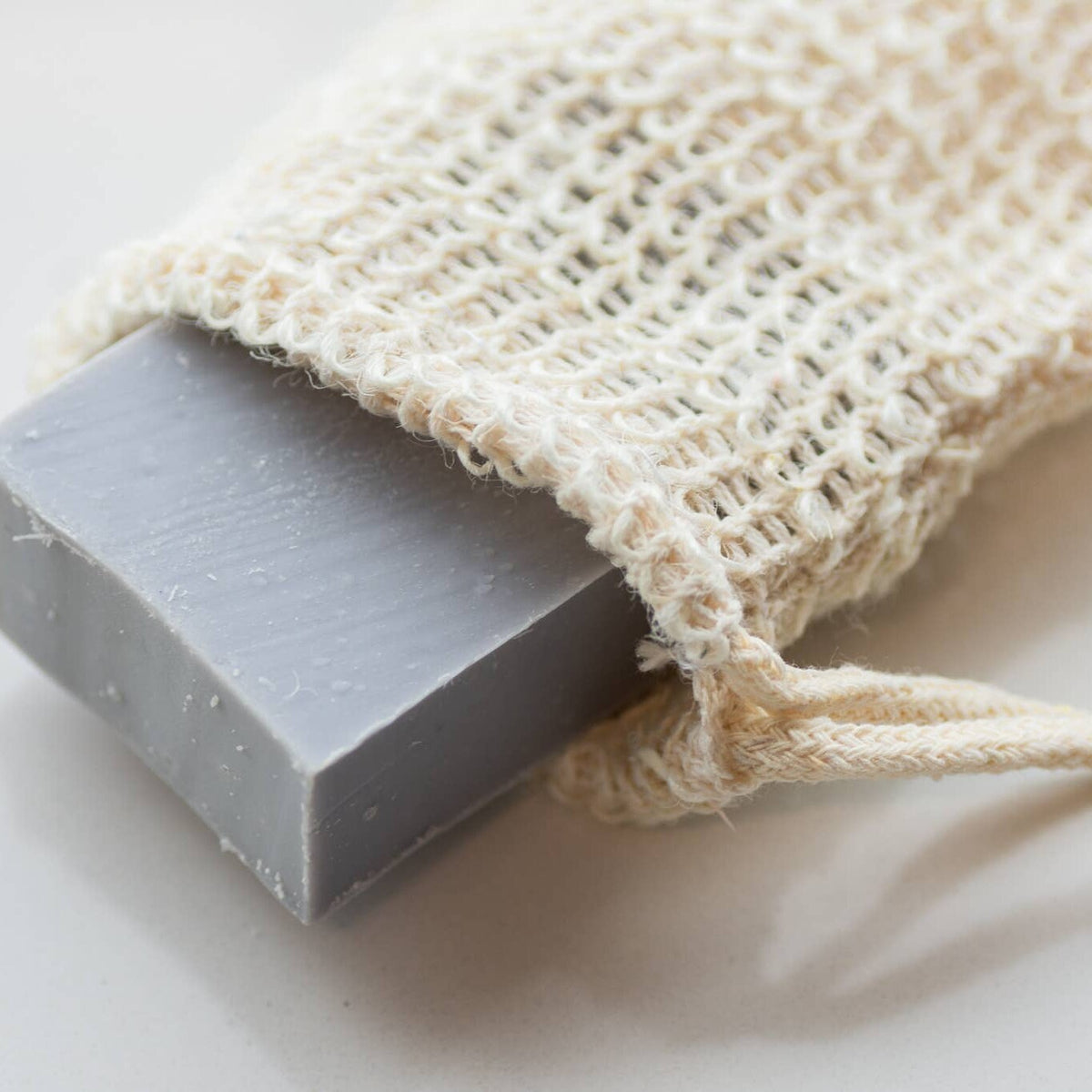 Close-up of a gray soap bar tucked inside a woven agave fiber soap bag