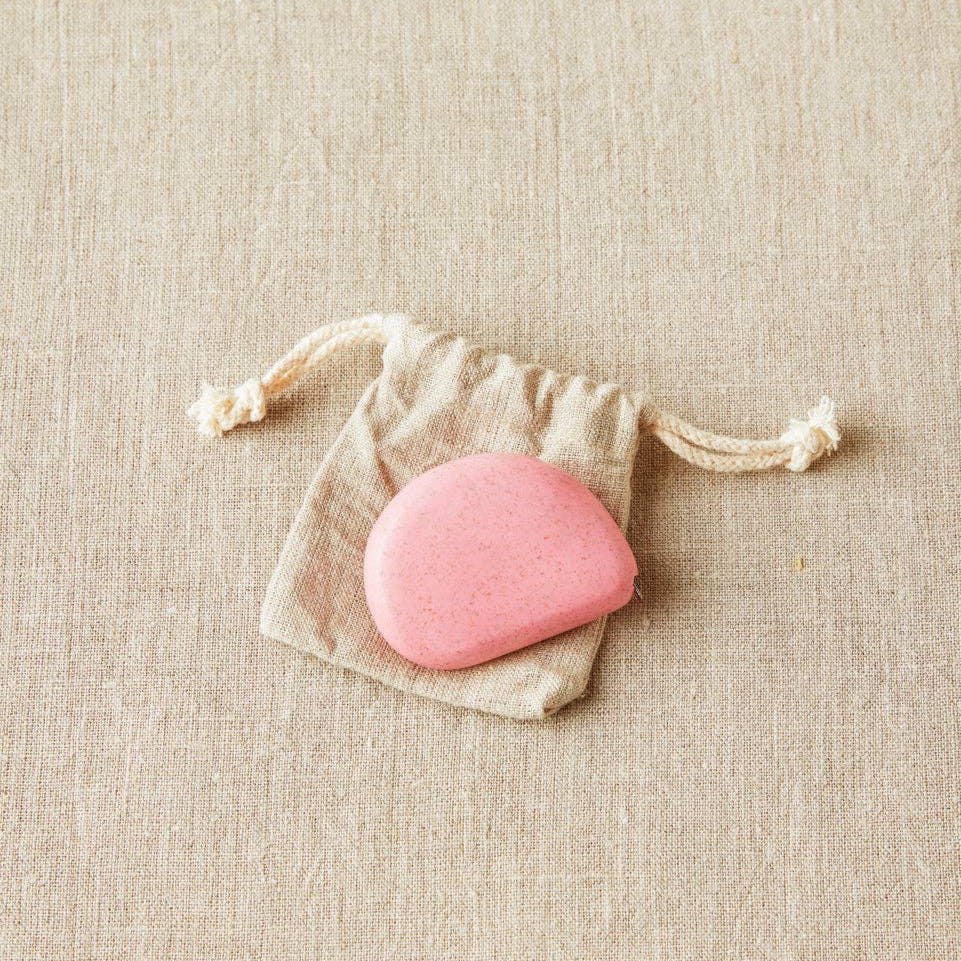 Hibiscus colored Cocoknits tape measure in a drawstring bag on a beige fabric background