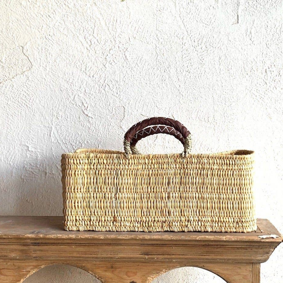 Woven basket with handles on a wooden surface against a white wall