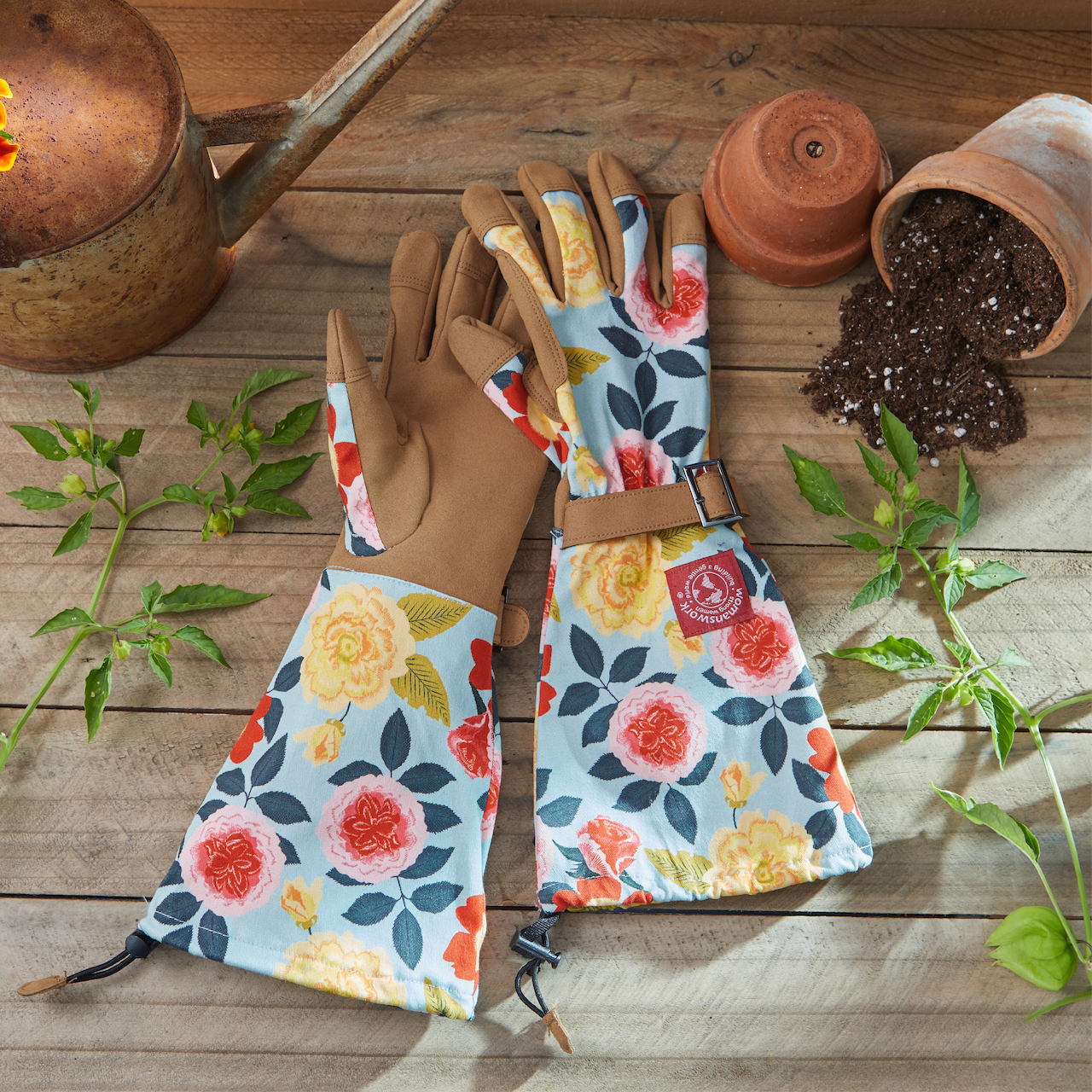 Gardening gloves with floral patterns on a wooden surface with plants and pots.