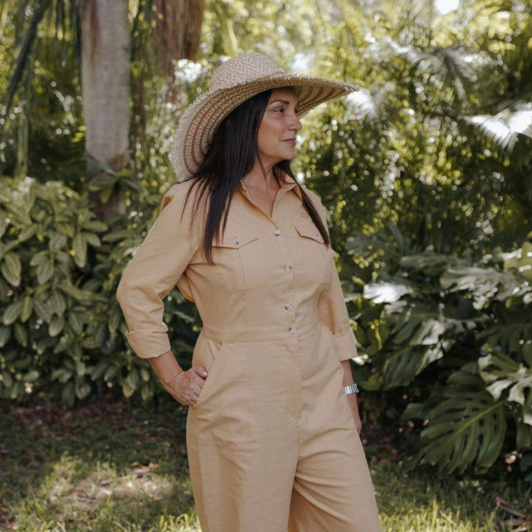 Person wearing a beige jumpsuit and hat standing in a garden